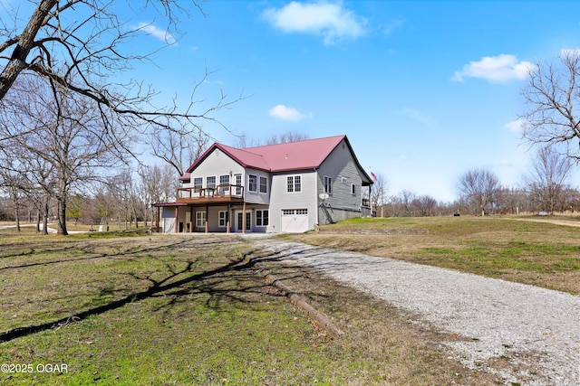 exterior space featuring dirt driveway, metal roof, a deck, a yard, and an attached garage