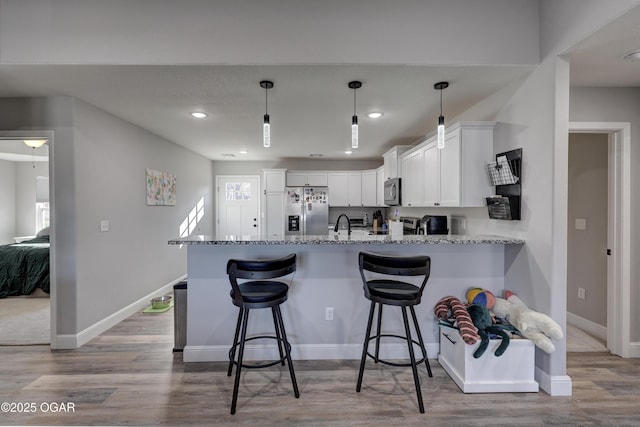 kitchen with light stone countertops, a peninsula, stainless steel appliances, wood finished floors, and white cabinetry