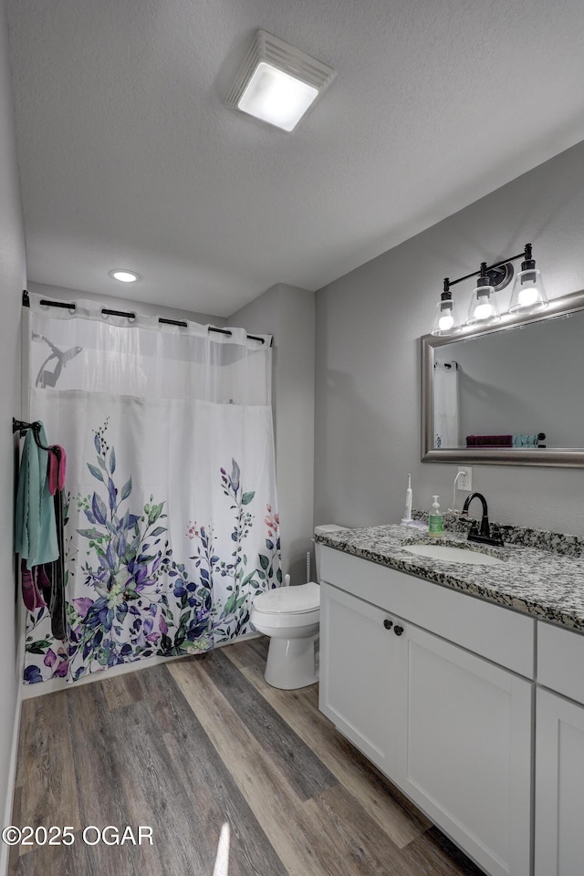 bathroom with toilet, a textured ceiling, wood finished floors, a shower with shower curtain, and vanity