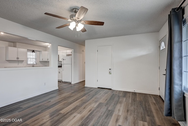 unfurnished living room featuring dark wood-type flooring, a sink, a textured ceiling, ceiling fan, and baseboards