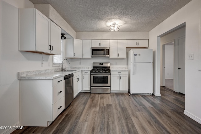 kitchen with appliances with stainless steel finishes, white cabinets, a sink, and dark wood-style floors