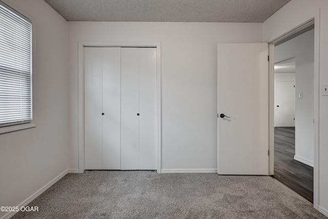 unfurnished bedroom featuring a textured ceiling, a closet, baseboards, and carpet flooring