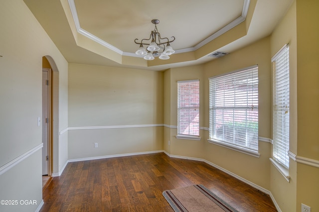 spare room with baseboards, arched walkways, wood finished floors, a tray ceiling, and crown molding