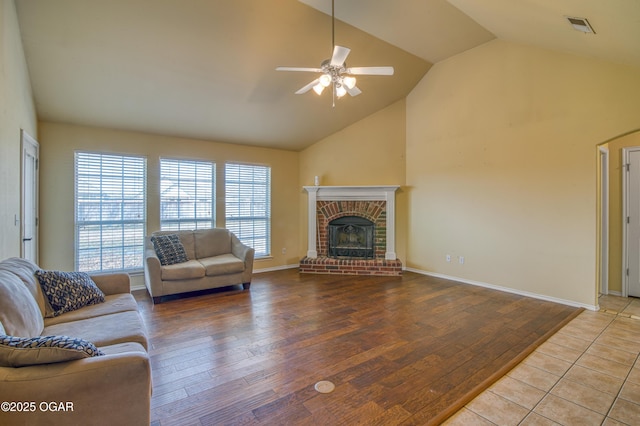 living area featuring ceiling fan, high vaulted ceiling, wood finished floors, visible vents, and a brick fireplace