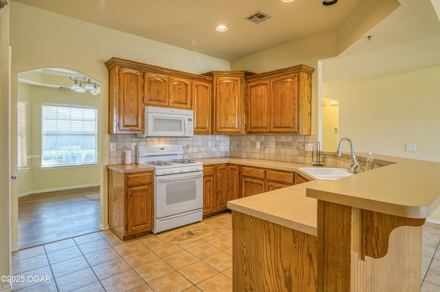 kitchen featuring light countertops, visible vents, a sink, white appliances, and a peninsula