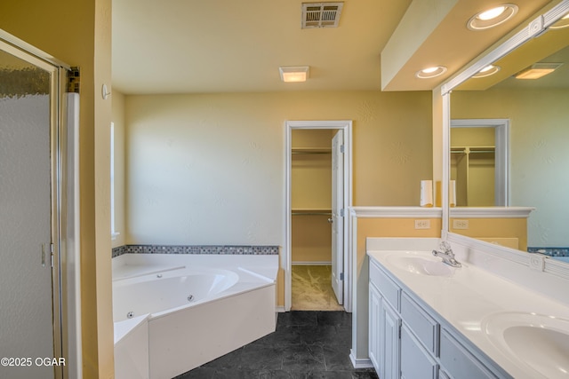 full bathroom featuring a sink, visible vents, double vanity, a tub with jets, and a walk in closet