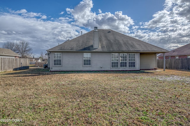 rear view of house with a yard, a shingled roof, a chimney, and a fenced backyard