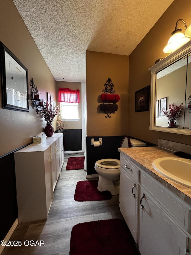 bathroom with toilet, a textured ceiling, wood finished floors, and vanity