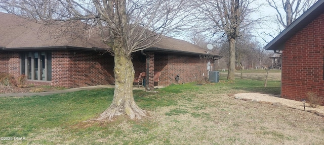 view of side of home with central air condition unit, a yard, a shingled roof, and brick siding