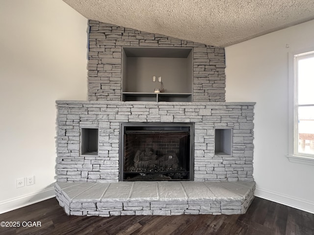 details featuring a textured ceiling, baseboards, wood finished floors, and a stone fireplace