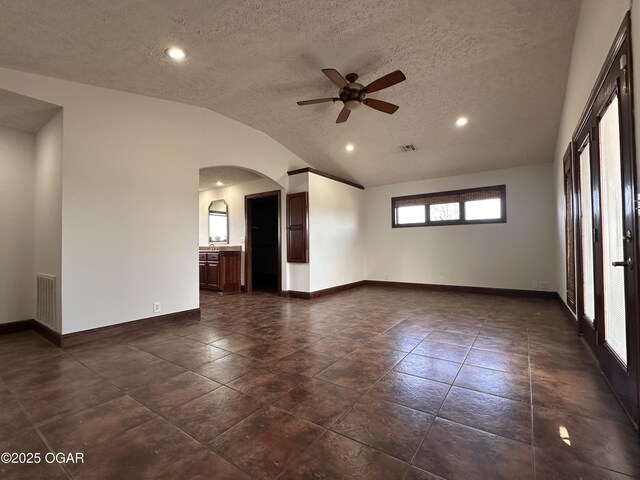 empty room featuring arched walkways, visible vents, vaulted ceiling, and baseboards