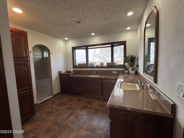 full bath featuring a textured ceiling, two vanities, a sink, and visible vents