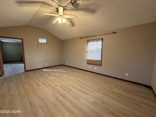 spare room with light wood finished floors, vaulted ceiling, and a textured ceiling