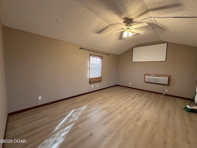 empty room with a wall mounted air conditioner, vaulted ceiling, a textured ceiling, and light wood finished floors