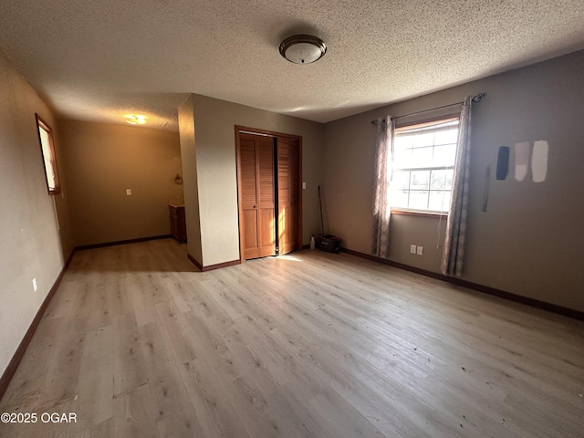 empty room featuring light wood-style floors, a textured ceiling, and baseboards