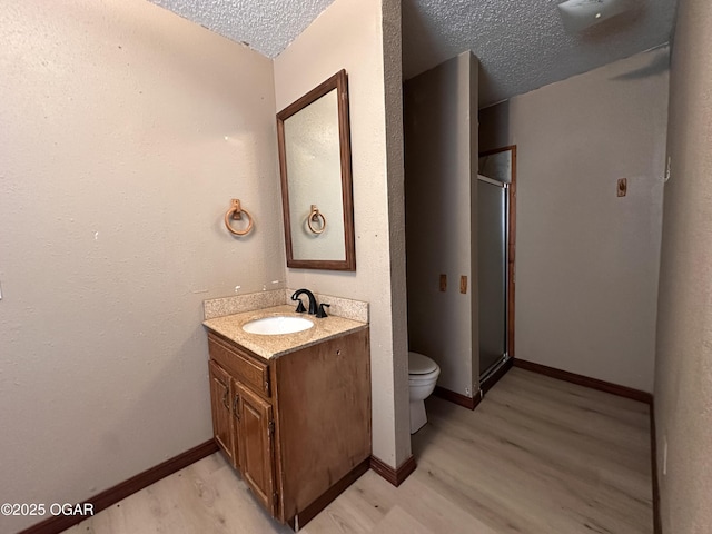 bathroom with toilet, a stall shower, a textured ceiling, vanity, and wood finished floors