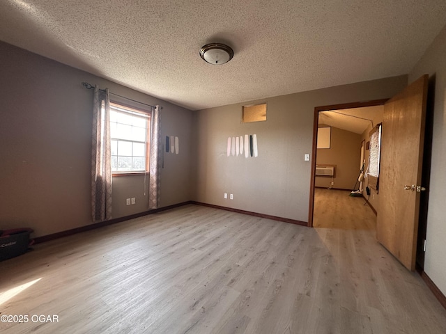 empty room featuring baseboards, light wood-style flooring, a textured ceiling, and a wall mounted AC