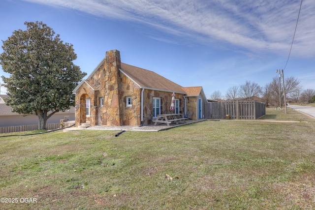 view of front of property featuring stone siding, a chimney, a front yard, and fence