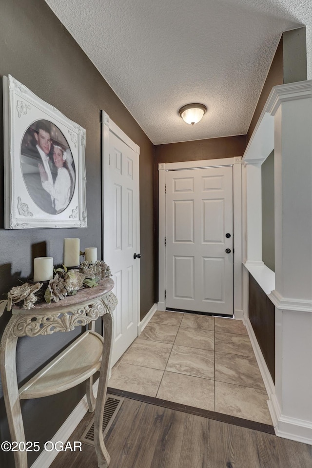 foyer with light wood-type flooring, visible vents, and a textured ceiling