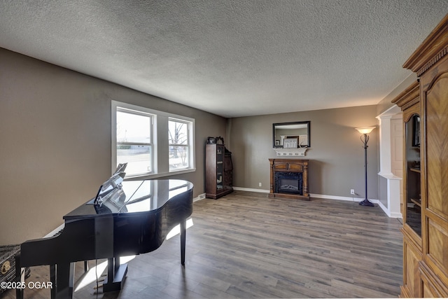 sitting room with a textured ceiling, baseboards, wood finished floors, and a glass covered fireplace