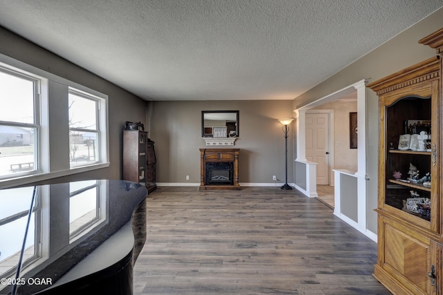 living area with a textured ceiling, baseboards, wood finished floors, and a glass covered fireplace