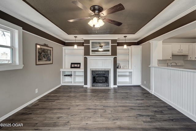 unfurnished living room with baseboards, a raised ceiling, dark wood-style floors, ceiling fan, and ornamental molding