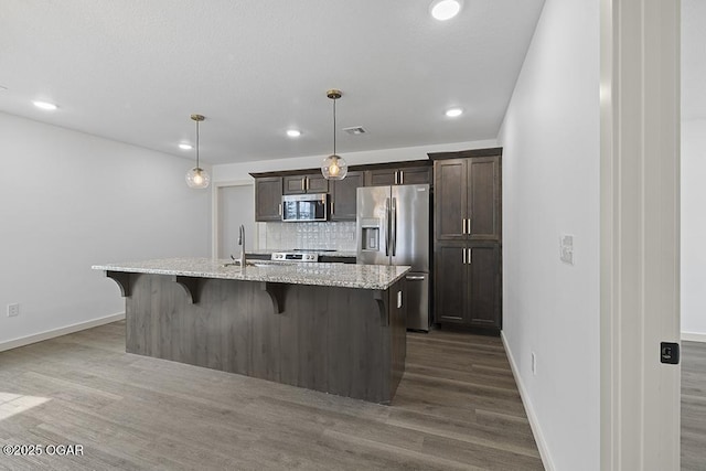 kitchen with dark brown cabinetry, a kitchen breakfast bar, a center island with sink, and appliances with stainless steel finishes