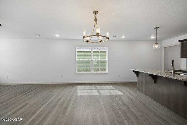 unfurnished dining area with a notable chandelier, a sink, wood finished floors, recessed lighting, and baseboards