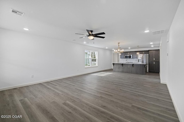 unfurnished living room with baseboards, visible vents, dark wood finished floors, recessed lighting, and ceiling fan with notable chandelier