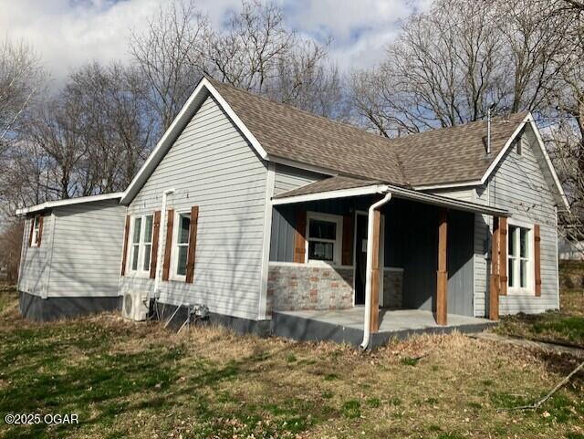 view of side of property with roof with shingles and a patio