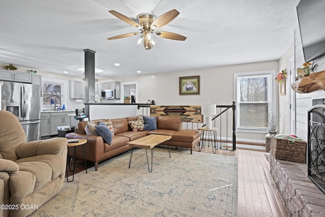 living area with a textured ceiling, hardwood / wood-style floors, recessed lighting, baseboards, and a brick fireplace