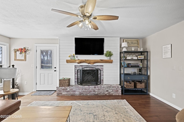 living room featuring baseboards, a textured ceiling, wood finished floors, and a fireplace