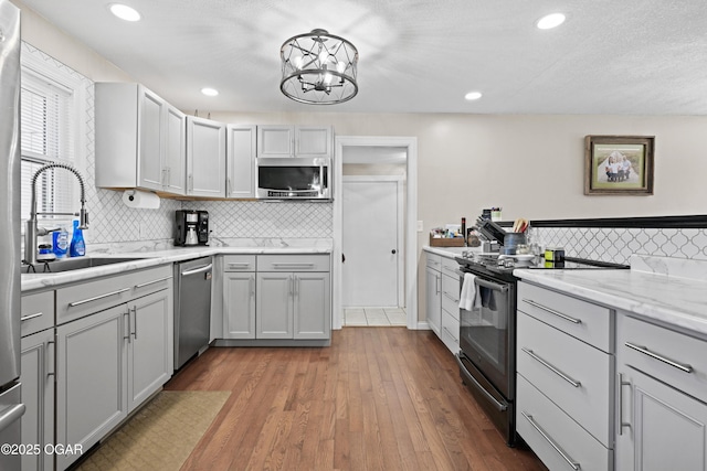 kitchen with a sink, backsplash, wood finished floors, recessed lighting, and appliances with stainless steel finishes