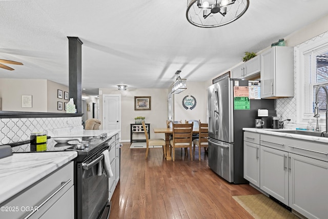 kitchen with electric range, ceiling fan with notable chandelier, a sink, dark wood-style floors, and stainless steel fridge