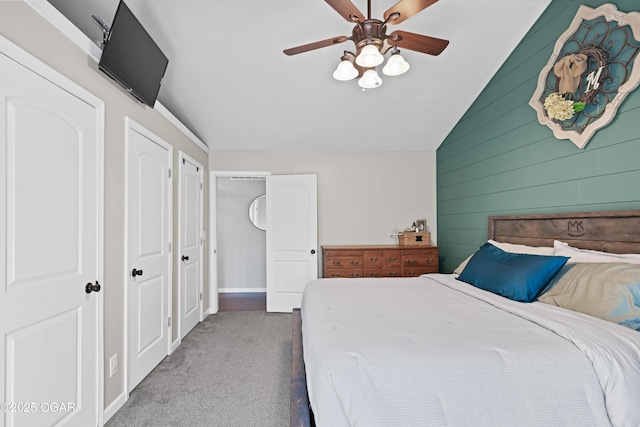 bedroom featuring wooden walls, baseboards, carpet, lofted ceiling, and a ceiling fan