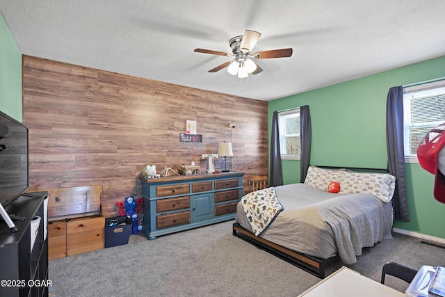 bedroom featuring a ceiling fan, carpet, wood walls, and a textured ceiling