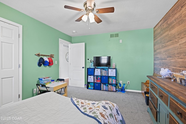 carpeted bedroom with visible vents, a ceiling fan, wood walls, baseboards, and an accent wall