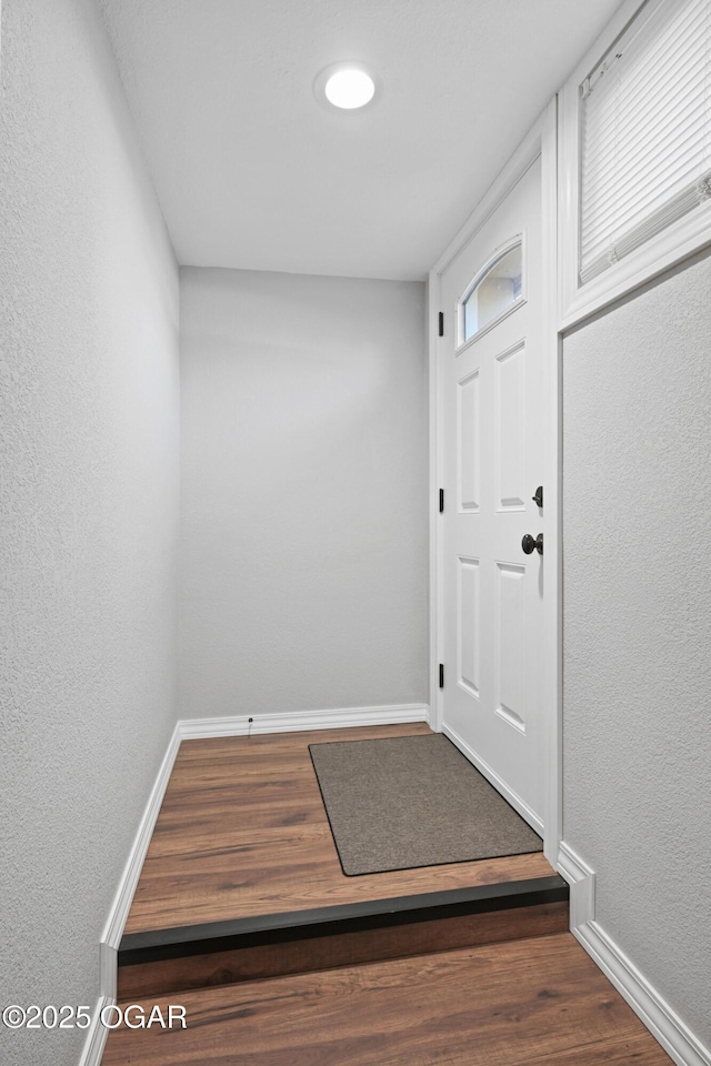 doorway with baseboards, wood finished floors, and a textured wall