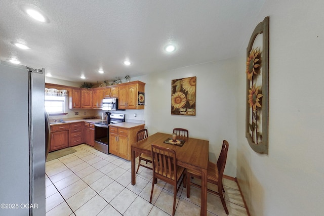 kitchen with light tile patterned floors, light countertops, appliances with stainless steel finishes, a textured ceiling, and brown cabinets