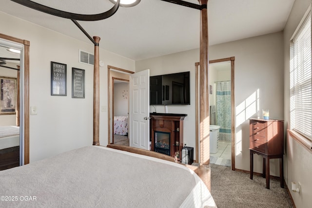 carpeted bedroom featuring visible vents, ensuite bath, and a glass covered fireplace