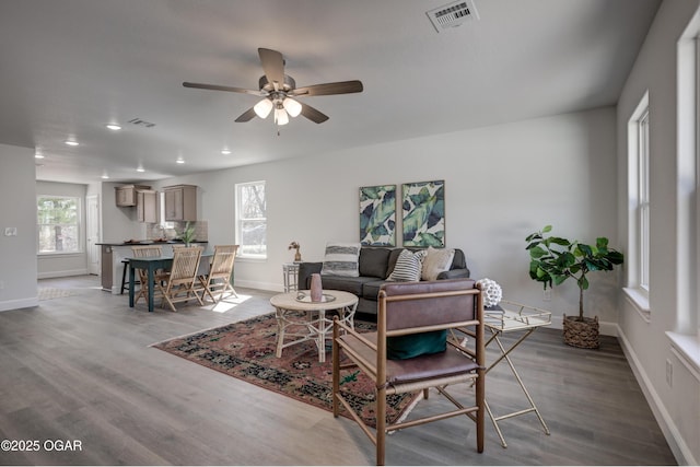 living area featuring visible vents, ceiling fan, baseboards, and wood finished floors