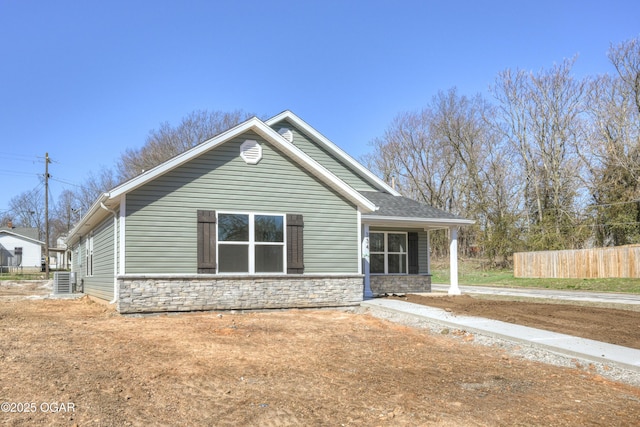 exterior space featuring stone siding, a shingled roof, and fence