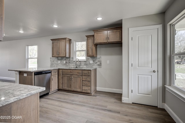 kitchen with tasteful backsplash, dishwasher, light wood-type flooring, a peninsula, and a sink