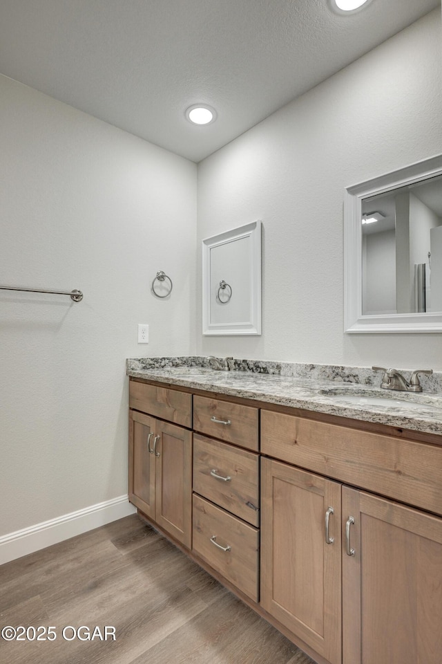 full bath featuring a sink, wood finished floors, baseboards, and double vanity