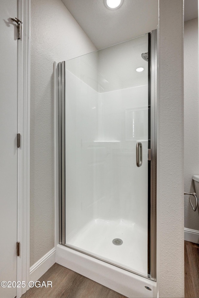 full bathroom with wood finished floors, a stall shower, a textured wall, and baseboards