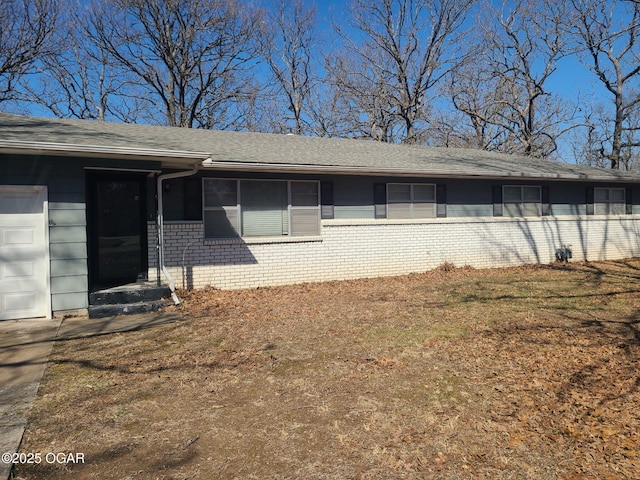 rear view of house with a garage, brick siding, and a shingled roof