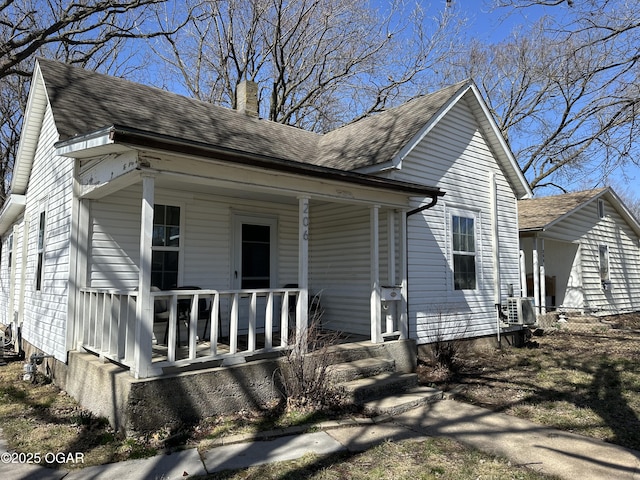 view of front facade with roof with shingles, a porch, and a chimney