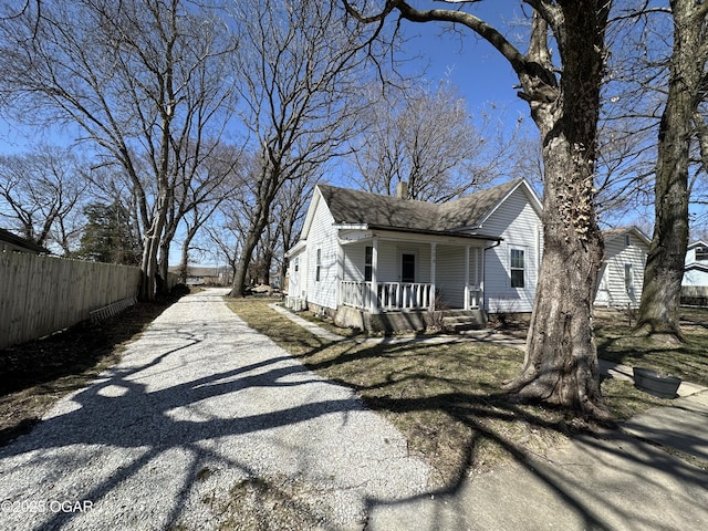 view of home's exterior featuring a shingled roof, gravel driveway, fence, covered porch, and a chimney