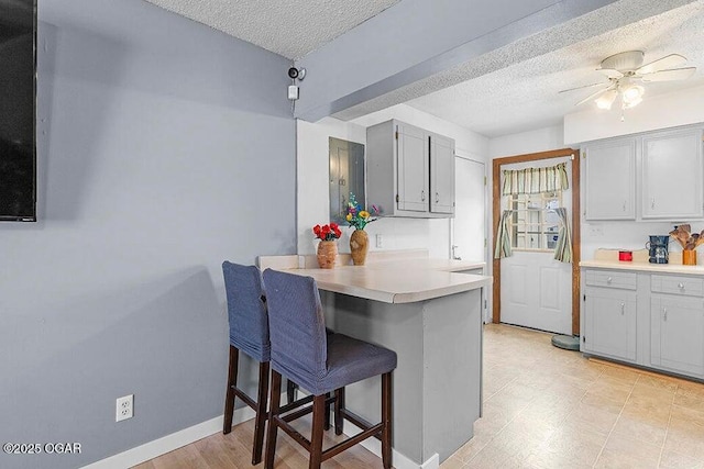 kitchen with baseboards, light countertops, a peninsula, a kitchen breakfast bar, and a textured ceiling