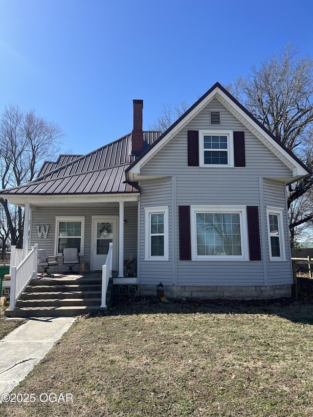 view of front of property featuring a standing seam roof, covered porch, a chimney, a front lawn, and metal roof